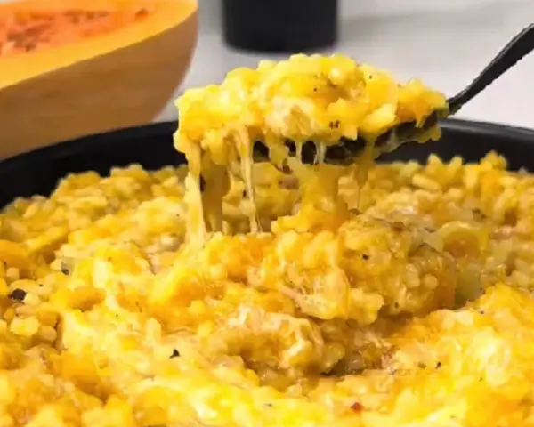 Risotto cremoso de calabaza en un plato, con una cuchara sacando una porción.