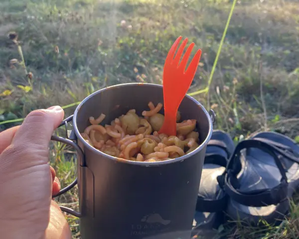 Un repas simple pour savoir que manger en randonnée : des pâtes avec des olives dans une tasse de camping, avec une fourchette orange.