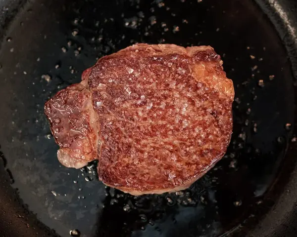 Ein saftiges Steak brutzelt in der Pfanne, bestreut mit grobem Salz.