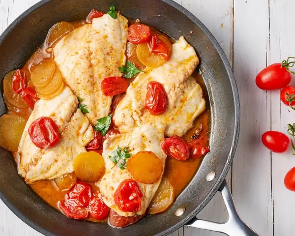 Deliziosi secondi di pesce in padella con pomodorini e patate, guarniti con prezzemolo fresco.