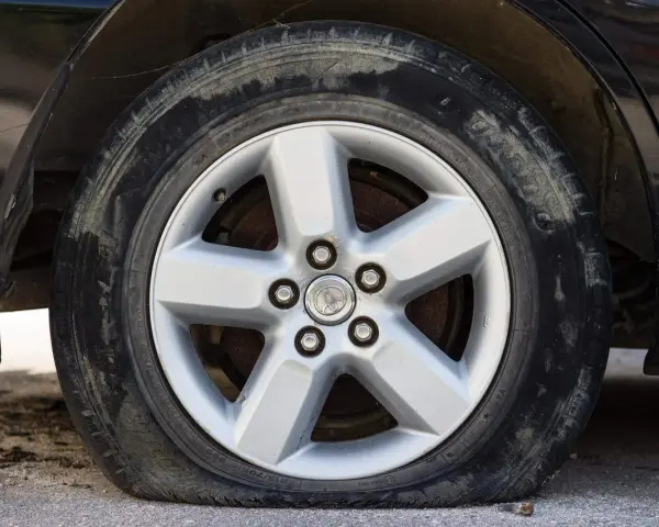 Ruota sgonfia dell'auto, con cerchione in lega a cinque razze e pneumatico sporco.