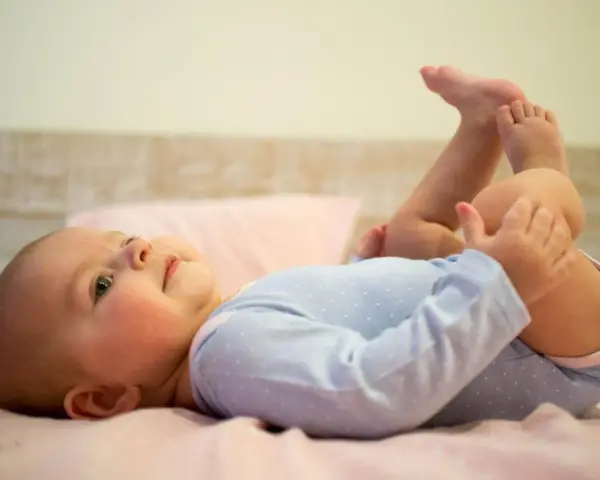 Uśmiechnięte, 5 miesięczne dziecko leży na plecach, podnosząc nóżki do góry.