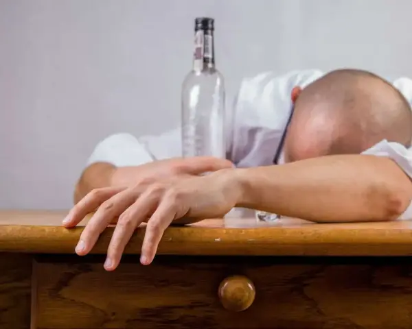 Bezradność i wyczerpanie. Pusta butelka i opuszczona głowa symbolizują mechanizmy obronne alkoholika, który pogrąża się w nałogu.