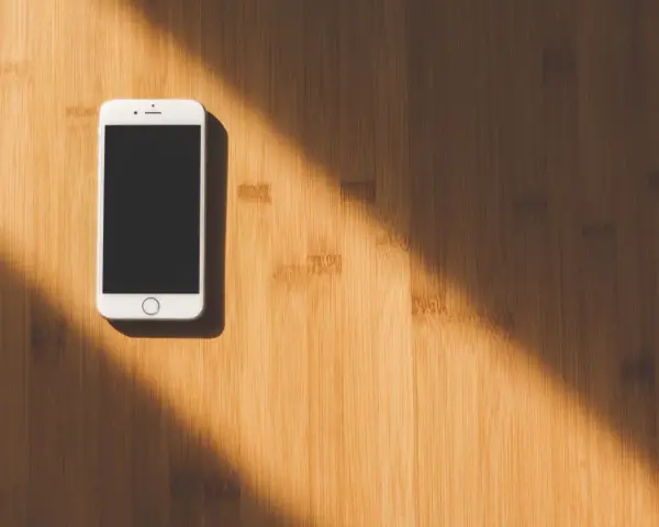 Biały smartfon leży na drewnianym blacie. Słońce rzuca cień. Jak namierzyć telefon, gdy zaginie?