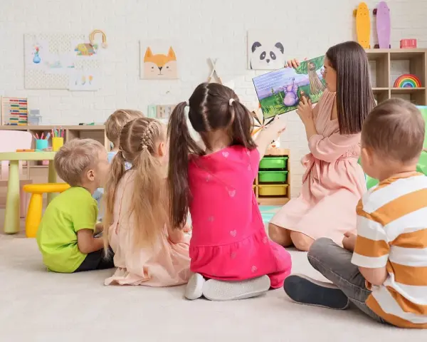 Nauczycielka czyta dzieciom bajkę. W przedszkolu bezpłatnych godzin jest 5.