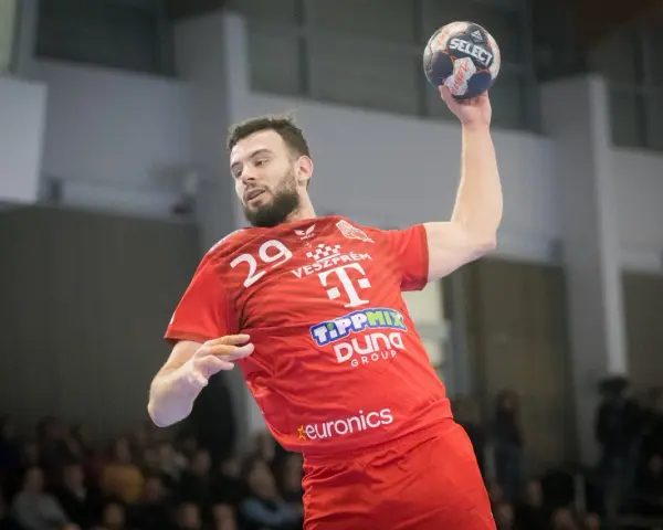 Piłkarz ręczny Nedim Remili w czerwonej koszulce z numerem 29, z piłką w dłoni, gotowy do rzutu.