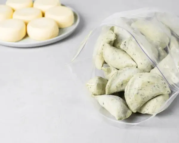 Mrożone pierogi w woreczku obok talerza z okrągłymi serkami.