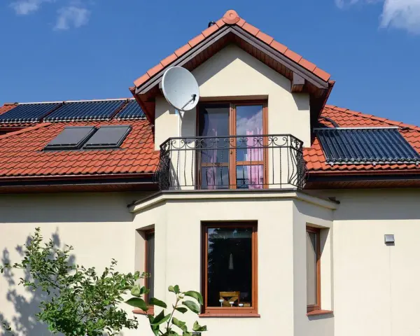 Nowoczesny wykusz w domu z balkonem i oknami, na dachu panele słoneczne i antenę satelitarną.