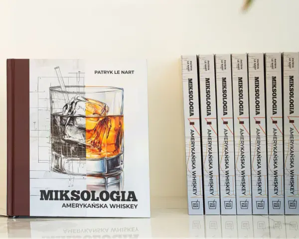 Książka "Miksologia Amerykańska Whiskey" Patryka Le Narta, z ilustracją szklanki z lodem i bursztynowym trunkiem. Obok niej rząd identycznych tomów.