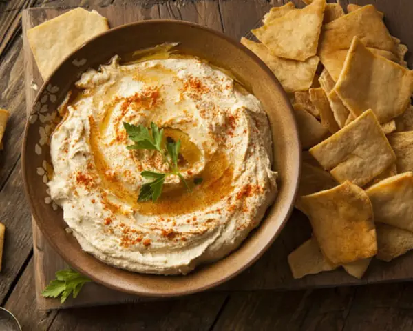 Houmous crémeux, garni de paprika et de persil, servi avec des chips pita croustillantes. Une recette houmous facile pour un apéritif gourmand.