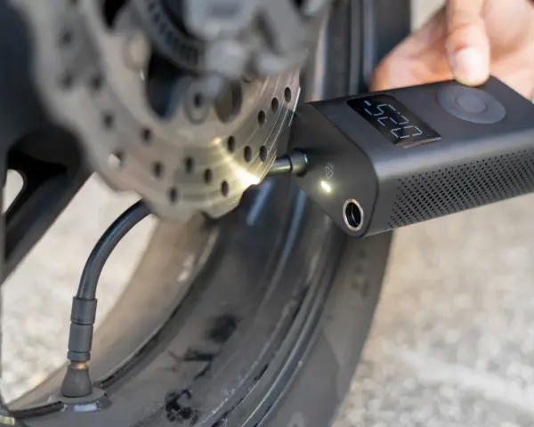 Gonfleur de pneu sans fil connecté à la valve d'une roue de moto, affichant la pression.