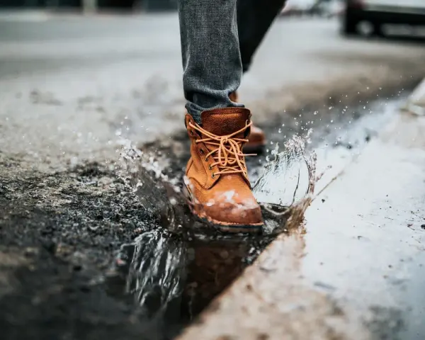 Botas de cuero marrón salpican un charco, demostrando que el cuero es impermeable.
