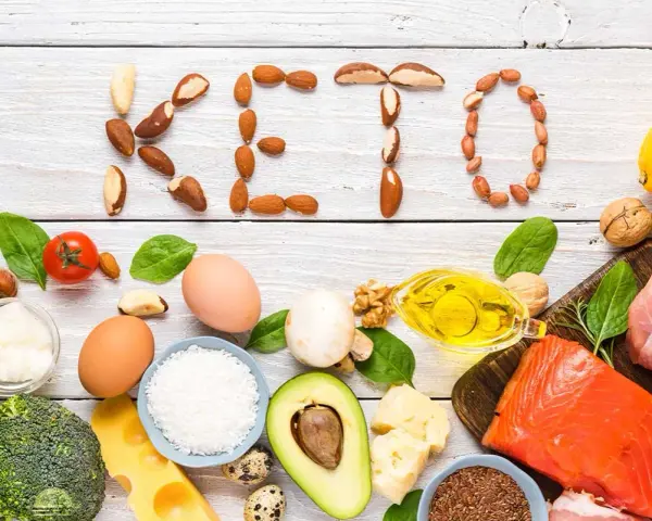 Słowa "KETO" ułożone z orzechów i nasion. Wokół składniki diety keto: ryba, mięso, jajka, awokado, olej, ser, warzywa.