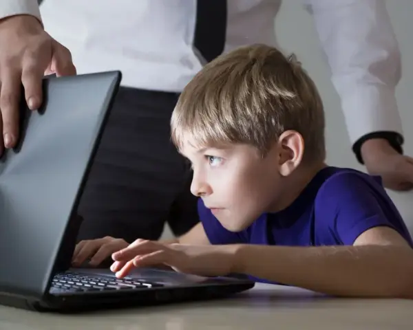 Chłopiec pochłonięty grą na laptopie, a dorosły próbuje pomóc w leczeniu uzależnienia od komputera.