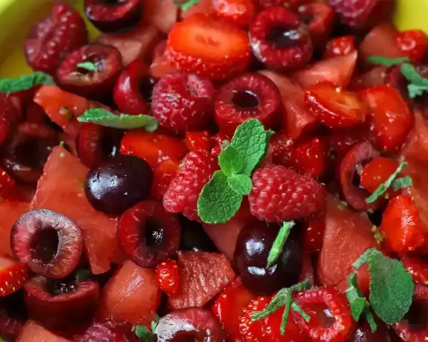 Macedonia di frutta fresca e colorata: fragole, ciliegie, lamponi e anguria, guarnita con foglie di menta.