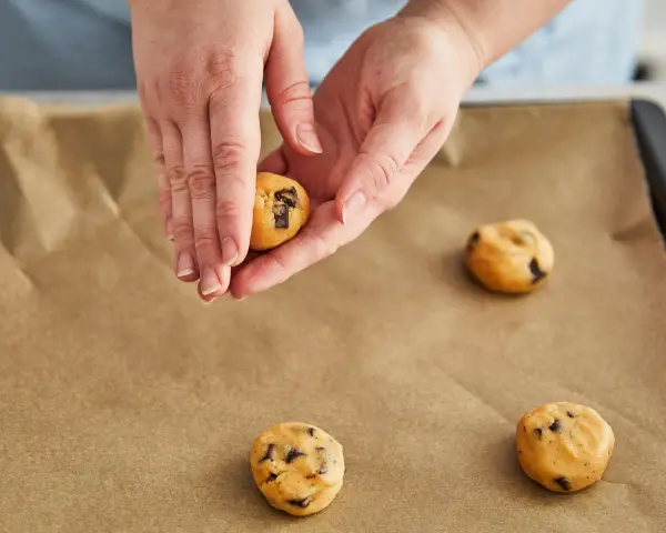 Hände formen Teig für einen Skillet Cookie mit Schokoladenstückchen auf Backpapier.
