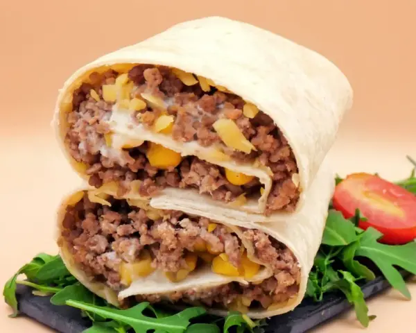 Pyszna tortilla z mięsem mielonym, kukurydzą i serem, przekrojona na pół, z rukolą i pomidorkiem.