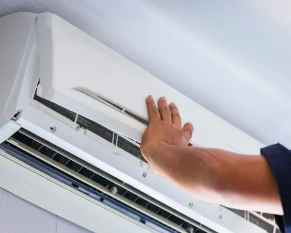 Ręka technika otwiera obudowę klimatyzatora do sprawdzenia szczelności.