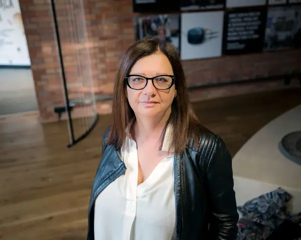 Małgorzata Szczęśniak w okularach i czarnej ramonesce, zamyślona.