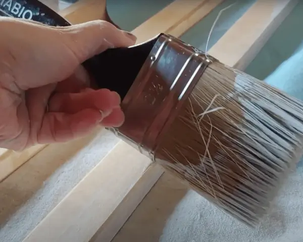 Mano aplica pintura con un pincel seco sobre listones de madera.