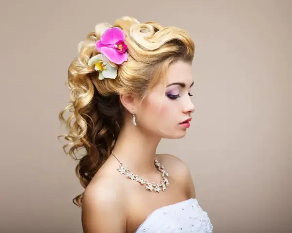 Elegancka, naturalna fryzura na wesele z lokami i kwiatami. Delikatne fale i ozdoby podkreślają urodę panny młodej.