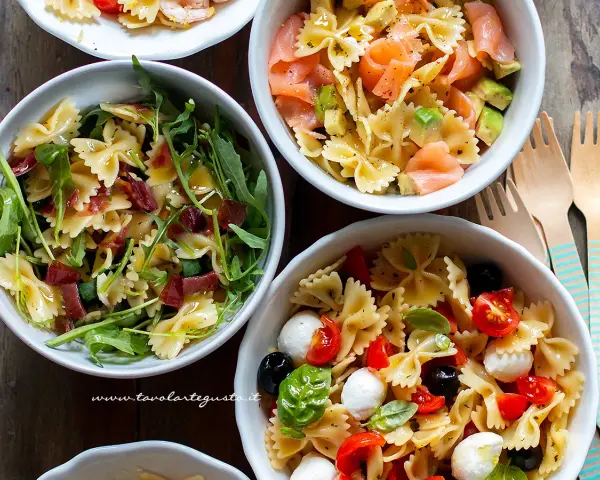 Tre ciotole di pasta fredda saporita: una con salmone e avocado, una con rucola e prosciutto, e una con pomodorini, mozzarelline e olive.