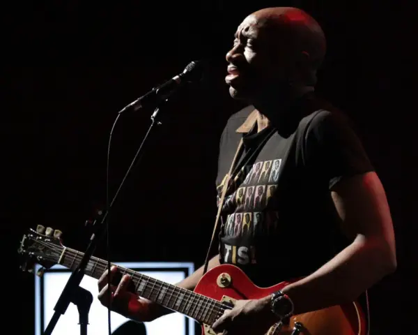 Musiker mit Gitarre und Mikrofon, trägt T-Shirt mit dem Titel von Otis Redding.