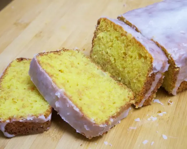 Un delicioso pastel de limón, cubierto con glaseado blanco, cortado en rebanadas sobre una tabla de madera.
