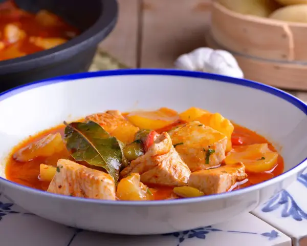 Bol de patatas con bonito en salsa roja, decorado con hojas de laurel.