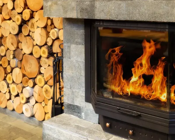 Leña apilada junto a una moderna insert chimenea con llamas danzantes.