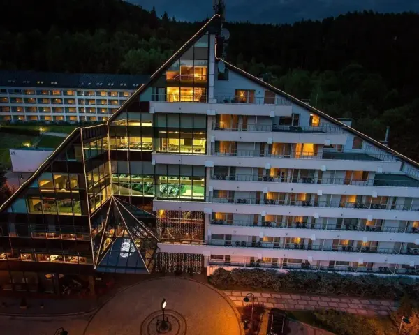 Nowoczesny hotel Klimczok Resort & Spa nocą, z oświetlonymi oknami i wejściem. Wiele pozytywnych hotel klimczok resort & spa opinie potwierdza jego urok.