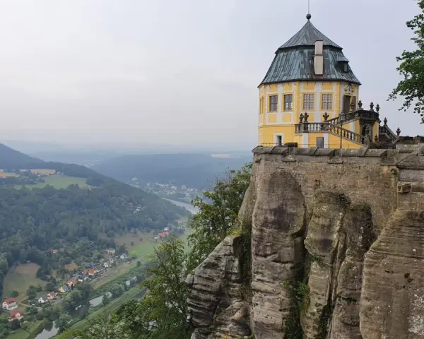 Żółty pałac na skale, część twierdzy Königstein, góruje nad doliną rzeki i lasami.