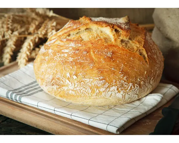 Ein knuspriges, schnelles Brot mit Backpulver, das auf einem karierten Tuch liegt. Im Hintergrund sind Ähren und ein Sack zu sehen.