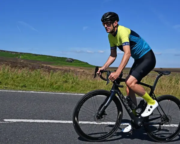Man cycling on max speed on a scenic road with hills in the background.
