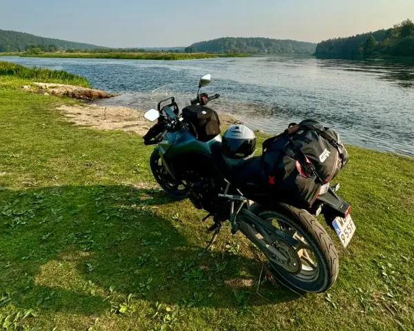 Motocykl z bagażem nad rzeką, gotowy do podróży po Litwie. Przepisy drogowe to podstawa bezpiecznej wyprawy.