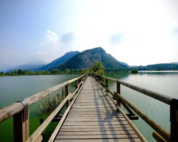Ponte in legno su lago calmo, montagne verdi sullo sfondo. Un luogo incantevole per scoprire cosa vedere in Franciacorta, tra natura e tranquillità.