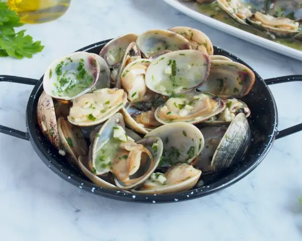 Almejas en salsa verde, un plato delicioso con mariscos frescos y perejil picado, listo para disfrutar.