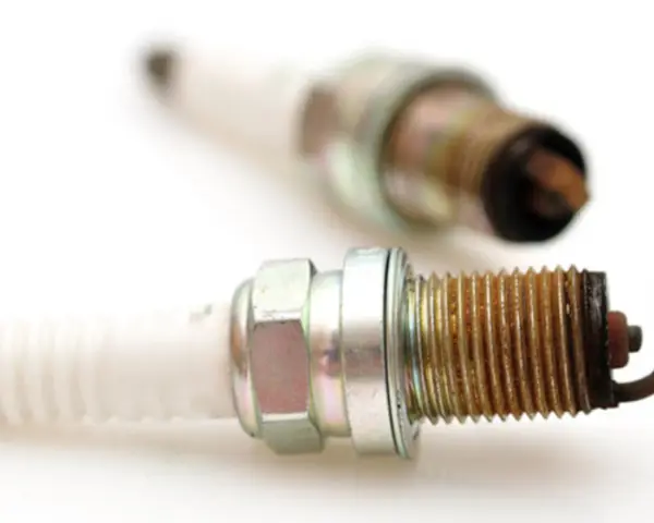 Two used spark plugs for cars, showing wear and tear on their metal tips.