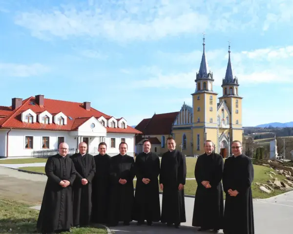Grupa księży w czarnych szatach przed żółtym kościołem. Czy to miejsce, gdzie zbierany jest podatek na kościół?