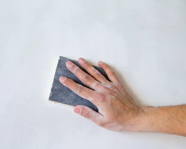 Mano che leviga una superficie bianca con carta vetrata per legno, quale usare per un lavoro perfetto.