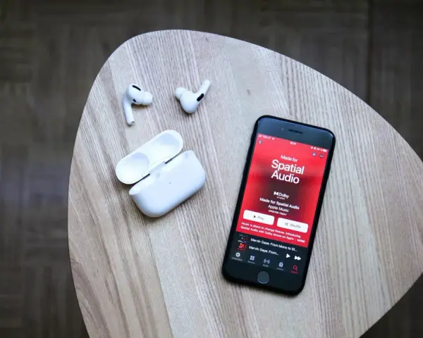 iPhone mit Apple Music Update zeigt "Made for Spatial Audio". AirPods und Ladecase liegen daneben.