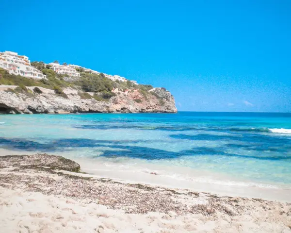 Plage de Majorque avec eaux turquoises, falaises et bâtiments blancs à flanc de colline.