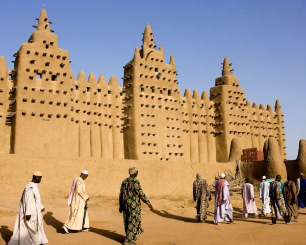 La grande mosquée de Djenné, chef-d'œuvre d'architecture en terre, se dresse sous un ciel bleu. Des hommes en tenues traditionnelles s'approchent, ajoutant vie à ce site historique.