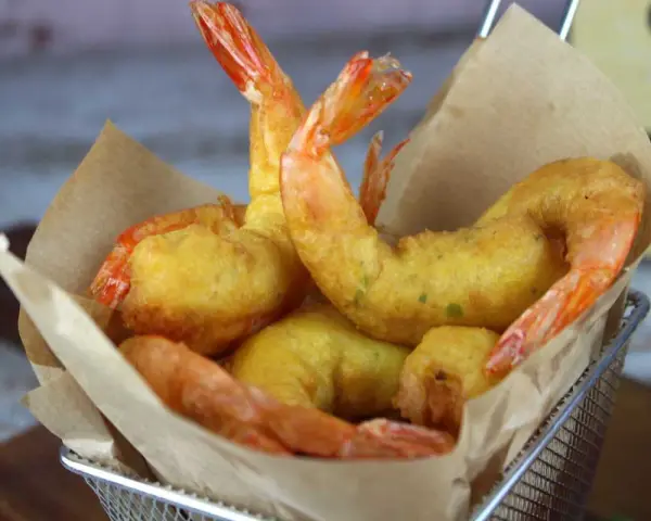 Crujientes gambas a la gabardina doradas y sabrosas, servidas en una cesta metálica con papel de cocina.