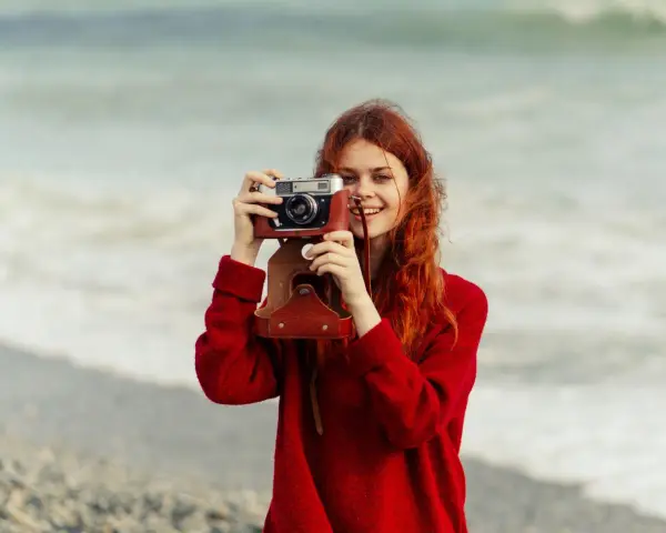 Ruda dziewczyna z aparatem, jak znani fotografowie, uwiecznia piękno morza.