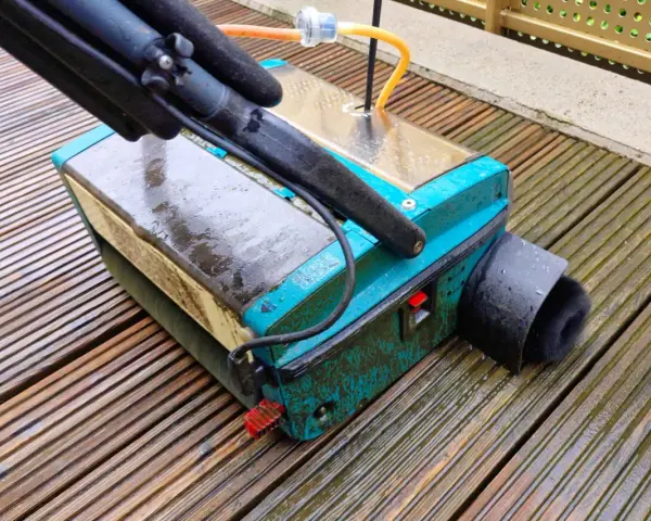 Gerät zur Bankirai Terrasse reinigen mit Bürstenaufsatz auf nassen Holzbrettern.