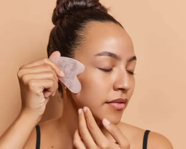 Frau mit geschlossenen Augen nutzt ein Gua Sha Stein zur Gesichtsmassage. Ob morgens oder abends, die Anwendung belebt die Haut.
