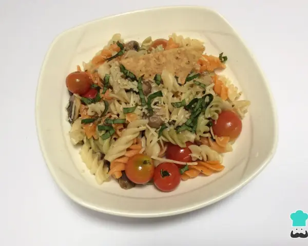 Pasta tricolor con tomates cherry, albahaca y queso rallado en un plato blanco.