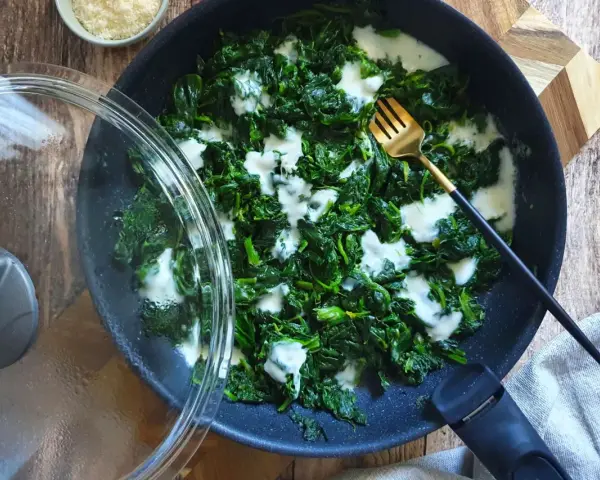 Spinaci in padella cremosi, con una forchetta dorata pronta ad assaggiarli. Un contorno semplice e gustoso.