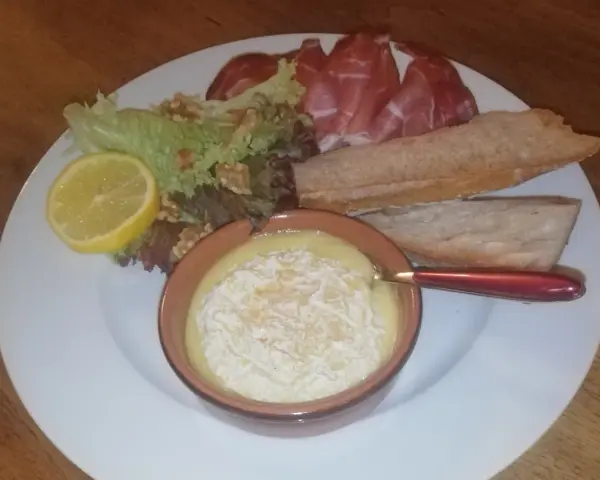 Un plat avec un fromage fondant, des tranches de jambon, de la salade, des noix, une tranche de citron et du pain. Une idée de recette amuse bouche facile sans cuisson.